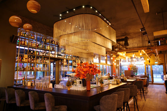 Innenraum einer Bar mit Getränkeregale, goldenem Kronleuchter, Lichterkette und gedeckten Tischen