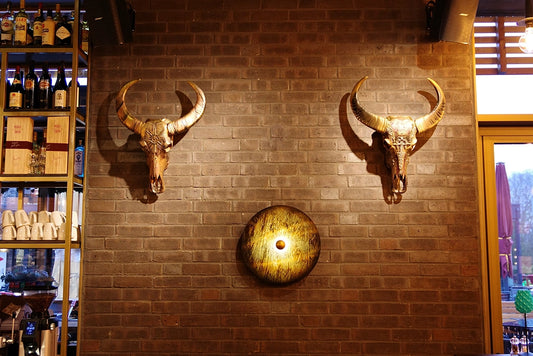 DINER XL innoLED Wandleuchte goldfarben mit Stierkopf-Design an Backsteinwand, runder Lichtpunkt